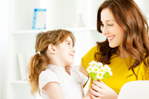 Portrait of an cute little girl, daughter, giving Bouquet of Daisies to her mother. Selective focus to little girl face and flowers.