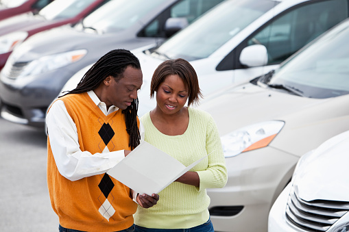African American couple shopping for new car at dealership.