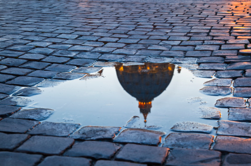 Dome in Vatican reflected in a puddle.Focus on cobblestone.