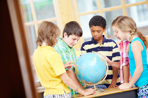 Happy group of young children pointing at countries on a world globe