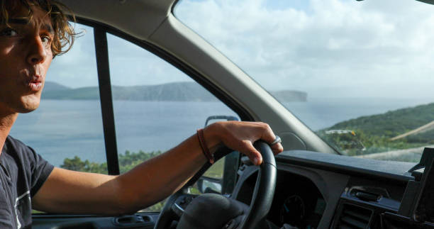Portrait of young man driving vehicle along seaside looking for surf