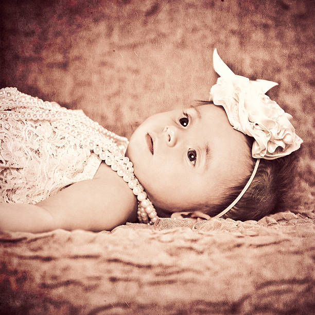 Portrait of an adorable 6 month old baby girl dressed in vintage attire looking up and away from the camera. Images has a texture and slight grain added.Image is processed from a 16 bit RAW file and profiled in ProPhoto RGB. All my images are professionally retouched.More from this series: