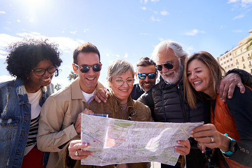 Group of diverse mature people smiling looking at a travel map on the street of a touristic city.