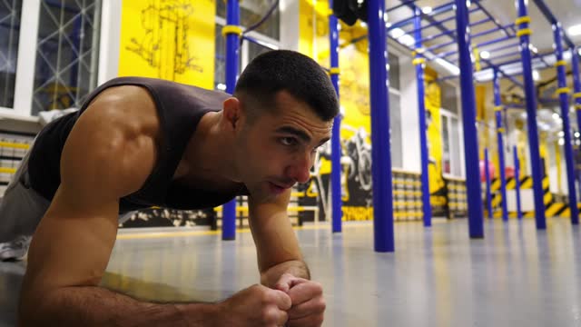 Strong sporty man doing a plank at modern gym. Young muscular sportsman strengthens his abdominal muscles at sport club. Athletic guy training in fitness centre. Concept of healthy lifestyle. Close up