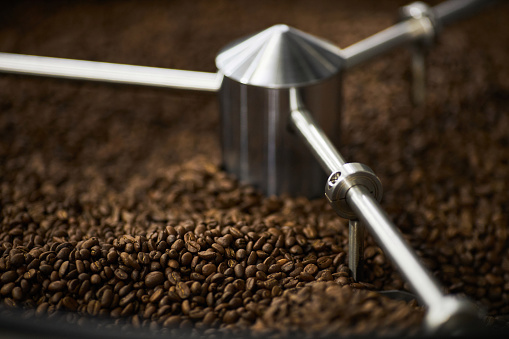 Close up background image of green coffee beans spinning in coffee roaster, copy space