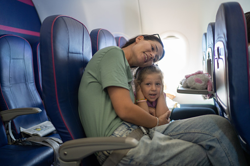 Cute little girl sitting in airplane with her mother, she is covering her ears.