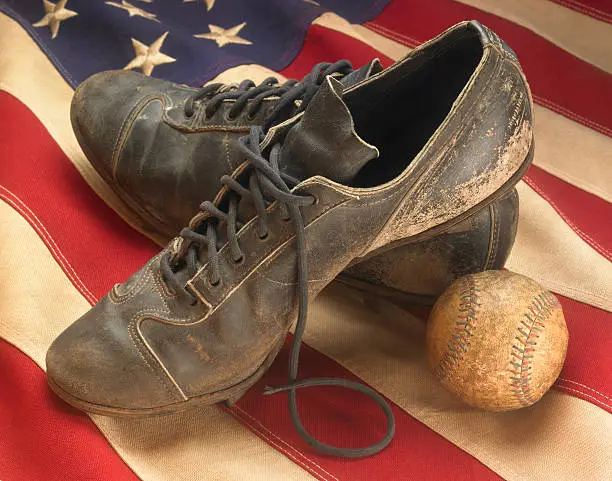 A pair of old weathered baseball cleats and an antique baseball, warmly lit on an American flag, and shot with a light soft focus filter to contribute to the nostalgic mood.