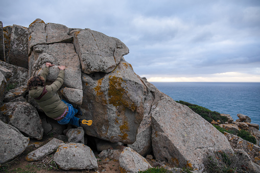 Young man scrambles up boulders above sea on stormy day