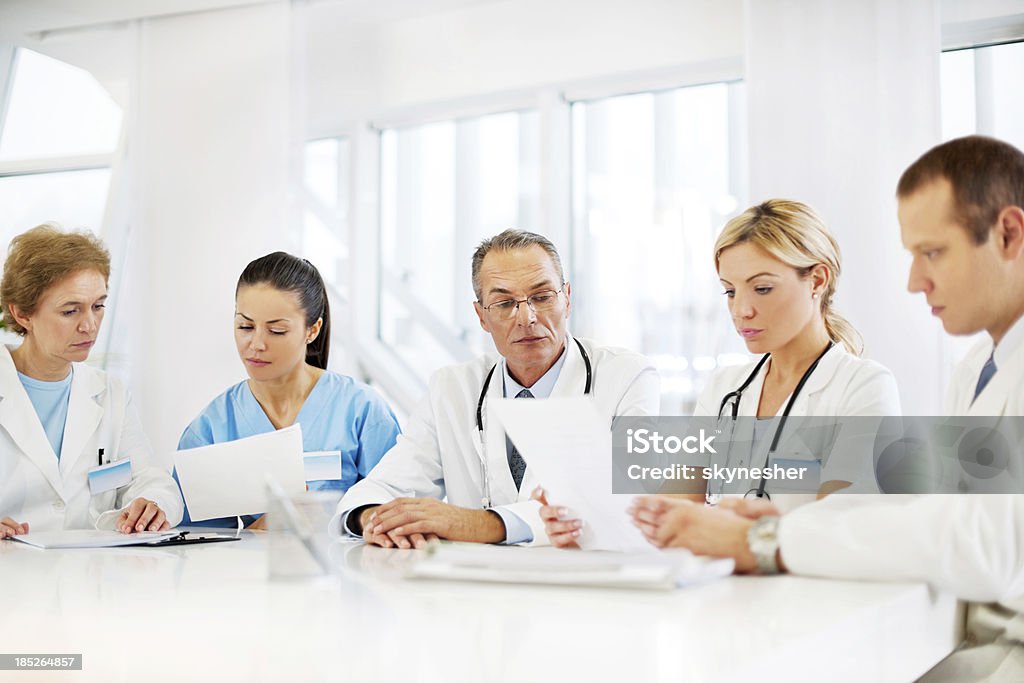 Team of doctors. Doctors working together.  They are sitting on a meeting and looking at the documents.  The focus is on the mature man wearing glasses.    Chart Stock Photo