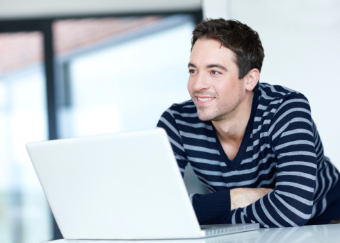 Young man smiling thoughtfully into the distance with his laptop in front of him - copyspace