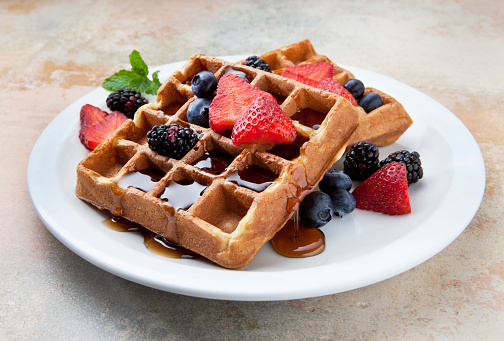 Close up big sweet traditional American or Belgian Brussels waffle with powder sugar and raspberry jam served on black slate board on table, elevated top view, directly above