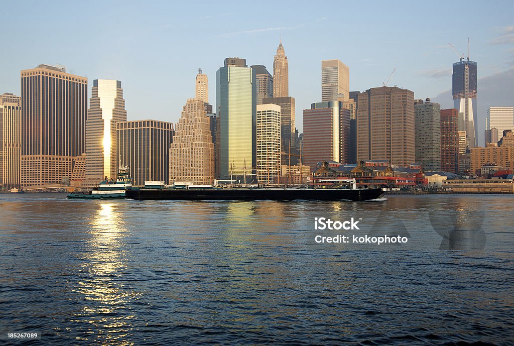 Barge in East River, NYC Financial District, Sunrise Tug Boat guiding a barge up the East River. Financial District buildings reflecting into calm waters of the East River. New York City Stock Photo