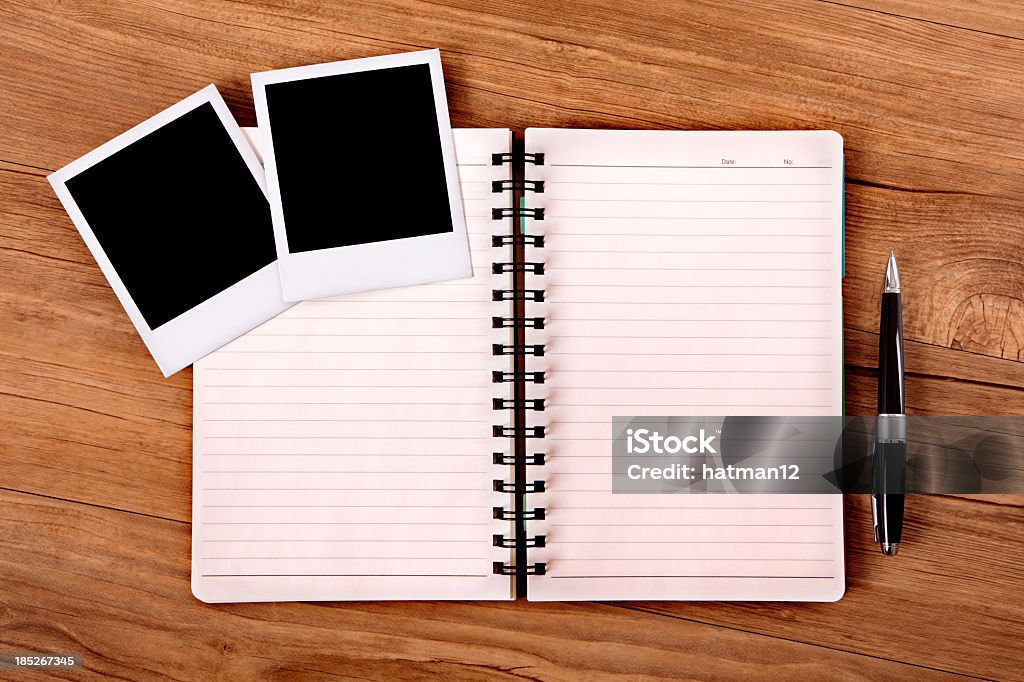 Wooden desktop with an open notebook, blank photos and a pen Desk or table with open notebook and two blank photo prints.  Paths provided.  Space for copy.  Alternative version shown below: Note Pad Stock Photo