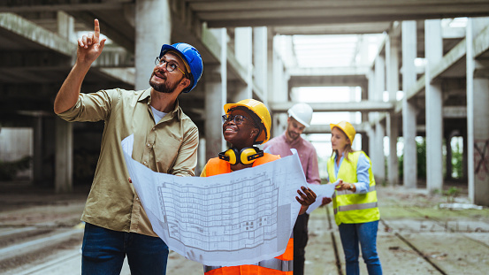 Construction concept of Engineer and Architect working at Construction Site with blue print. Group of construction engineer team in standard safety uniform work planing in construction site