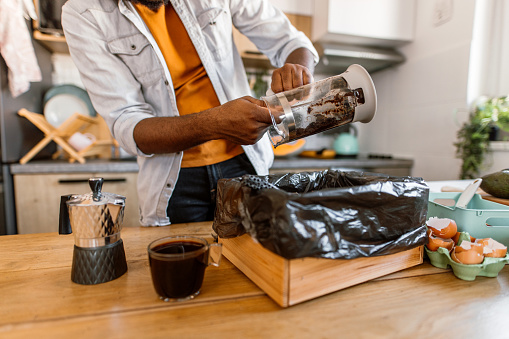 Young man preparing a coffee and cleaning used coffee grounds from coffee pot. Putting organic coffee waste in compost bin.