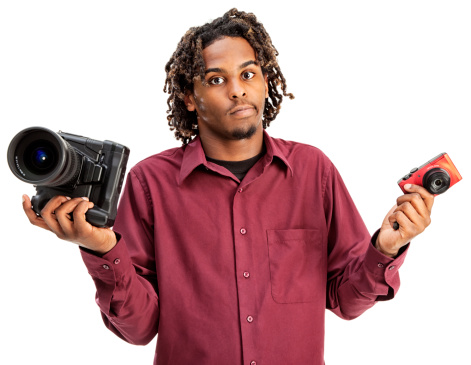 Photo of a young African Amercan man perplexed by the decision over which type of camera best suits him; isoalted on white.