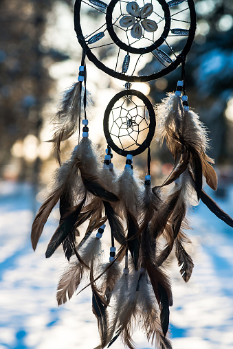 Dreamcatcher, spiritual protection amulet with feathers on sunset background. Boho style.