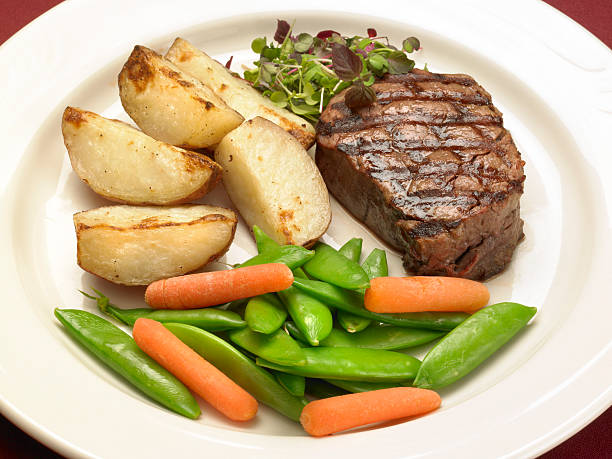 Close-up of a juicy fillet steak on a white plate. Includes potatoes and vegetables.