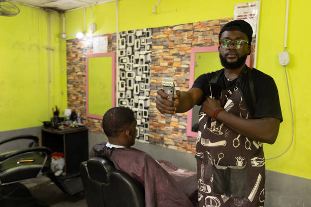A barber in his barbershop holds a razor while his customer looks at himself in the mirror A barber in his barbershop holds a razor while his customer looks at himself in the mirror. black barber stock pictures, royalty-free photos & images