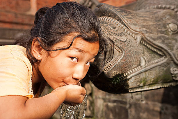 Young Nepali girl drinking from city fountain on Durbar Square "Young Nepali schoolgirl drinking from city fountain (founded by King Veer Deva in 299 A.D.) on Durbar Square Patan, Nepal. Patan Durbar Square has been listed by UNESCO as one of seven Monument Zones that make up the Kathmandu Valley World Heritage Site." developing countries photos stock pictures, royalty-free photos & images