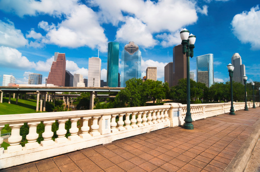 View of Downtown Houston's skyline with a historic bridge over the Buffalo Bayou and historic lampposts in the foreground.