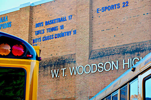 Fairfax, Virginia, USA - November 18, 2023: Large “W.T. Woodson High School” sign on the side of the school’s auditorium as seen through school busses waiting to take children home for the day.