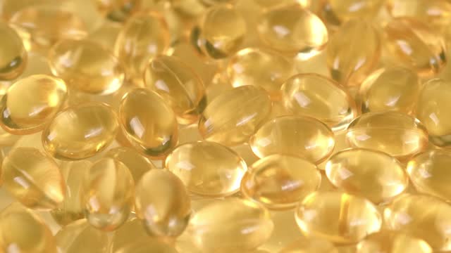 liquid Omega-3 in yellow transparent capsules, rotating closeup nutritional supplements and vitamins