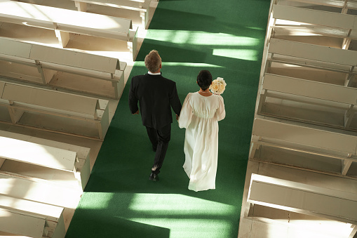 Top view at senior couple walking down aisle in church during wedding ceremony in sunlight, copy space