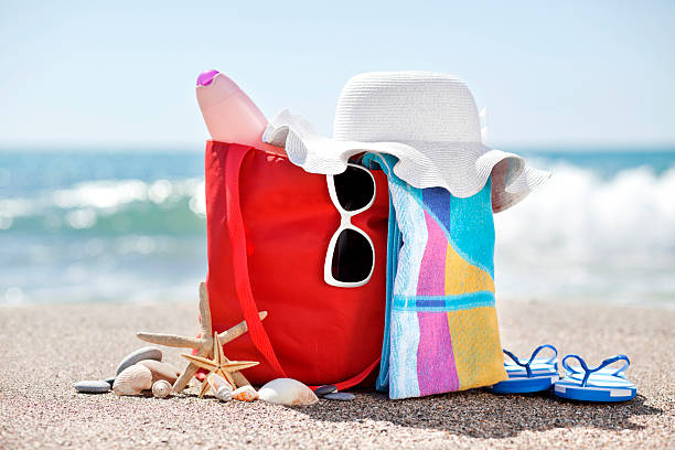 Holiday concept "Beach bag with hat,towel, sunglasses, sun lotion, pebbles, seashells and flip flops at the beach" beach bag stock pictures, royalty-free photos & images