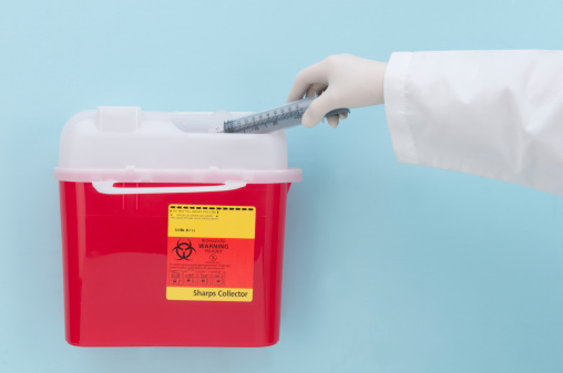 This image show the proper method of disposing of a biologically hazardous needle and syringe in a wall mounted Sharp's container.