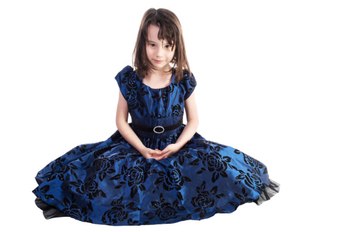 Six year old girl in party dress and messy hair sitting on floor.  Horizontal studio shot on white.
