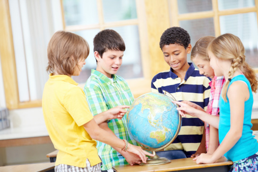 Group of young children smiling while pointing at countries on a world globe