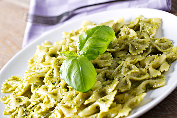 A classic Italian dish, Tagliatelle al Pesto Genovese, elegantly plated in a white bowl. The pasta is coated in a rich, homemade basil pesto sauce, garnished with toasted pine nuts and freshly grated Parmesan cheese. The dark background and minimalist presentation highlight the dish’s vibrant green color and creamy texture. This gourmet Italian meal represents the authentic flavors of Ligurian cuisine, making it perfect for food photography, restaurant branding, and fine dining promotions.
