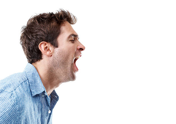 Dramatic portrait of angry Asian young man in casual shirt scolding loudly with hand movements making hand claws. Dark ambience conceptual image
