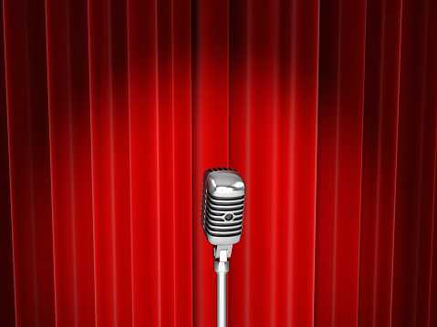 An old style microphone on stage in front of red velvet curtains.