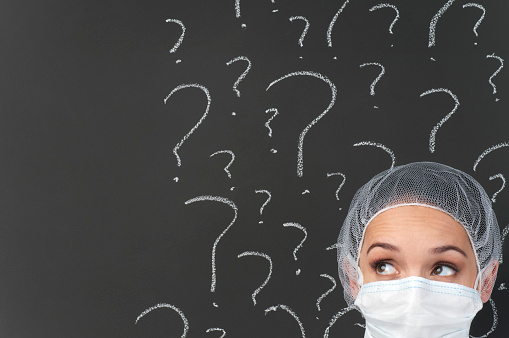 Female doctor thinking in front of question marks on blackboard with copy space