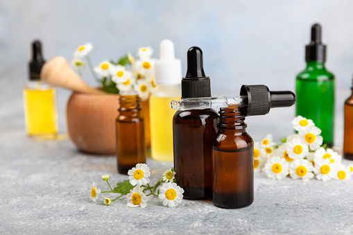 Glass bottle with chamomile essential oil on wooden background. Chamomile flowers, close up. Aromatherapy, spa and herbal medicine ingredients. Beauty concept.Copy space. Natural cosmetic