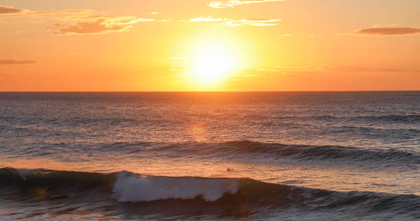 Scenic view of distant surfer at sunset