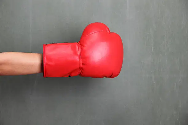 Arm with red boxing glove against green blackboard