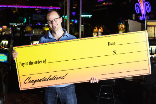 A smiling man holds a blank giant check inside a casino.