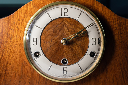 Vintage chiming mantel clock, close up photo, front view. White clock face with Arabic numerals in wooden case