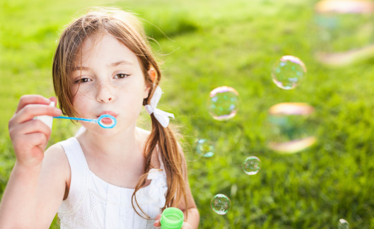 Beautiful little girl blowing bubbles on a summer day. Horizontal Shot.