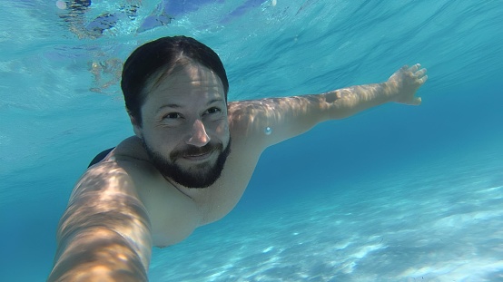 A man swimming in a clear blue pool of ocean water, arms forward in an upward position