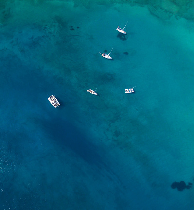 Top aerial view of catamarans and sailing yachts at shallow anchorage.