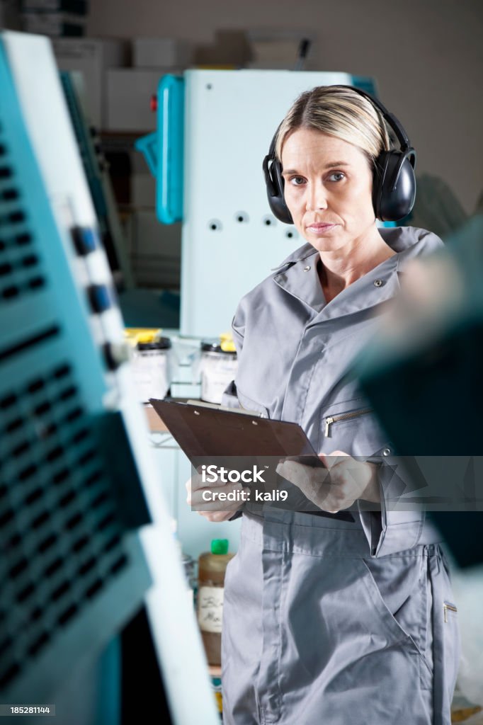 Female worker at printing plant Mature woman (40s) standing next to printing press. Ear Muff Stock Photo