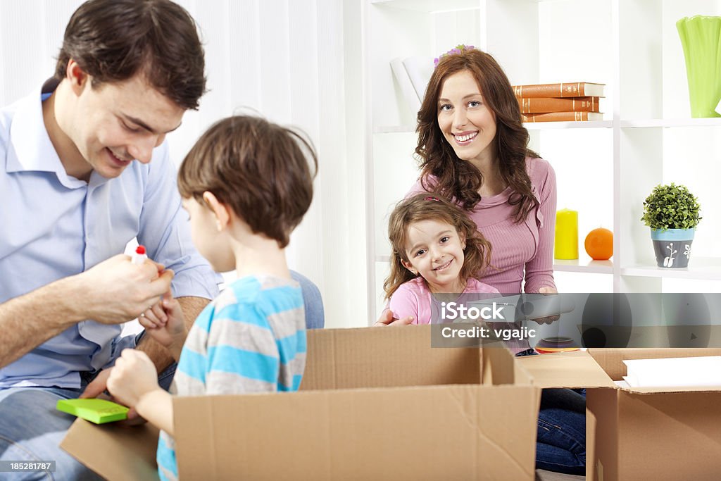 Family Moving Into New House Family with two children packing/unpacking boxes and moving to new house, selective focus to mother and daughter packing books into boxes. 30-39 Years Stock Photo