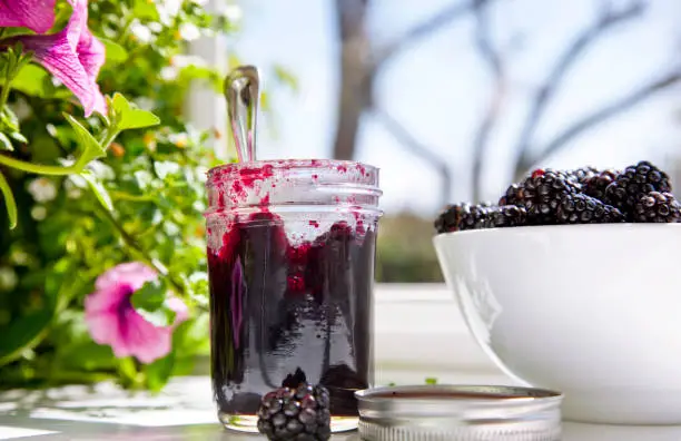 Black raspberry jam in a glass jar by the window.
