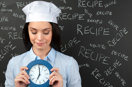 Female chef with clock front of recipe words on blackboard