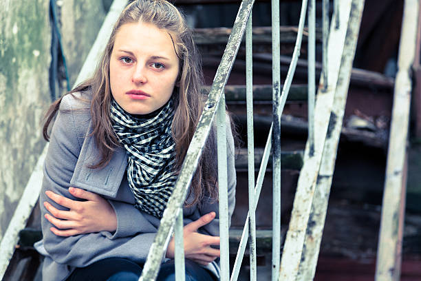 Outdoor image of Asian, sad girl looking down, thinking and sitting on steps in hilly area. She is in torn jeans and tank top. One person, three quarter length, horizontal composition with copy space.
