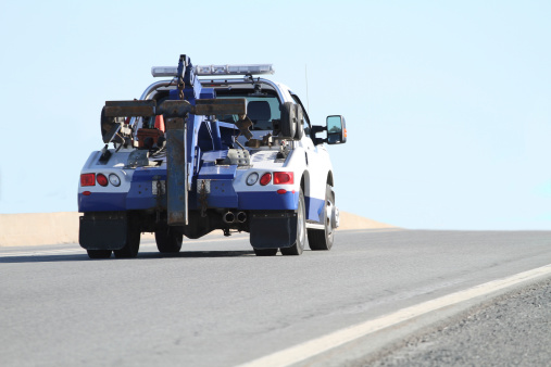 Rear quarter view of a nondescript tow truck travelling on a highway.  Shallow dof with focus on rear of truck. Slight motion blur.